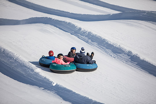 People sledding in innertubes on a snowy hill.